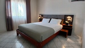 A neatly made bed with a wooden frame, a headboard with a dark finish, and two bedside tables with lamps. - Palm Beach Vacation Villa (Noord)