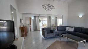 A spacious living area with a large flat-screen TV, a sectional sofa, and a coffee table. - Palm Beach Vacation Villa (Noord)