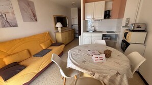 Espaço compacto com sofá, mesa de jantar, área de cozinha e um pequeno armário.