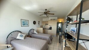 A compact hotel room with two beds, a kitchenette, a ceiling fan, a small dining table, and a bookshelf. - Cozy apartment with balcony, pets allowed, for holidays or treatments (Balaruc-les-Bains)