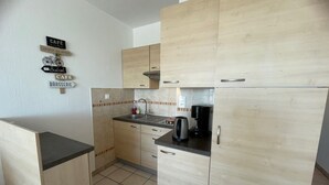 A compact kitchen with light wood cabinets, a black countertop, and a coffee maker. - Cozy apartment with balcony, pets allowed, for holidays or treatments (Balaruc-les-Bains)