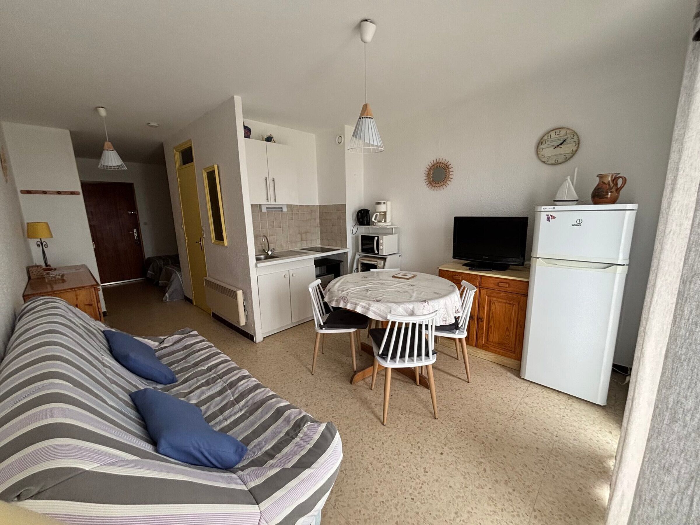 A compact living space with a kitchenette, a dining area, and a sofa with pillows.