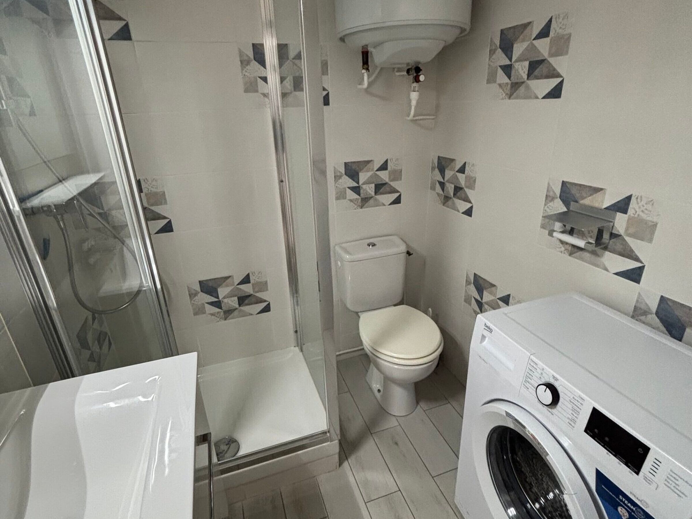 A bathroom with a glass shower enclosure, a toilet, and a washing machine.