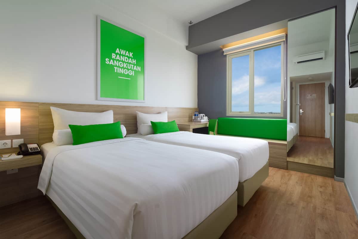 Een hotelkamer met twee bedden, een groene wand, een raam en een spiegel.
