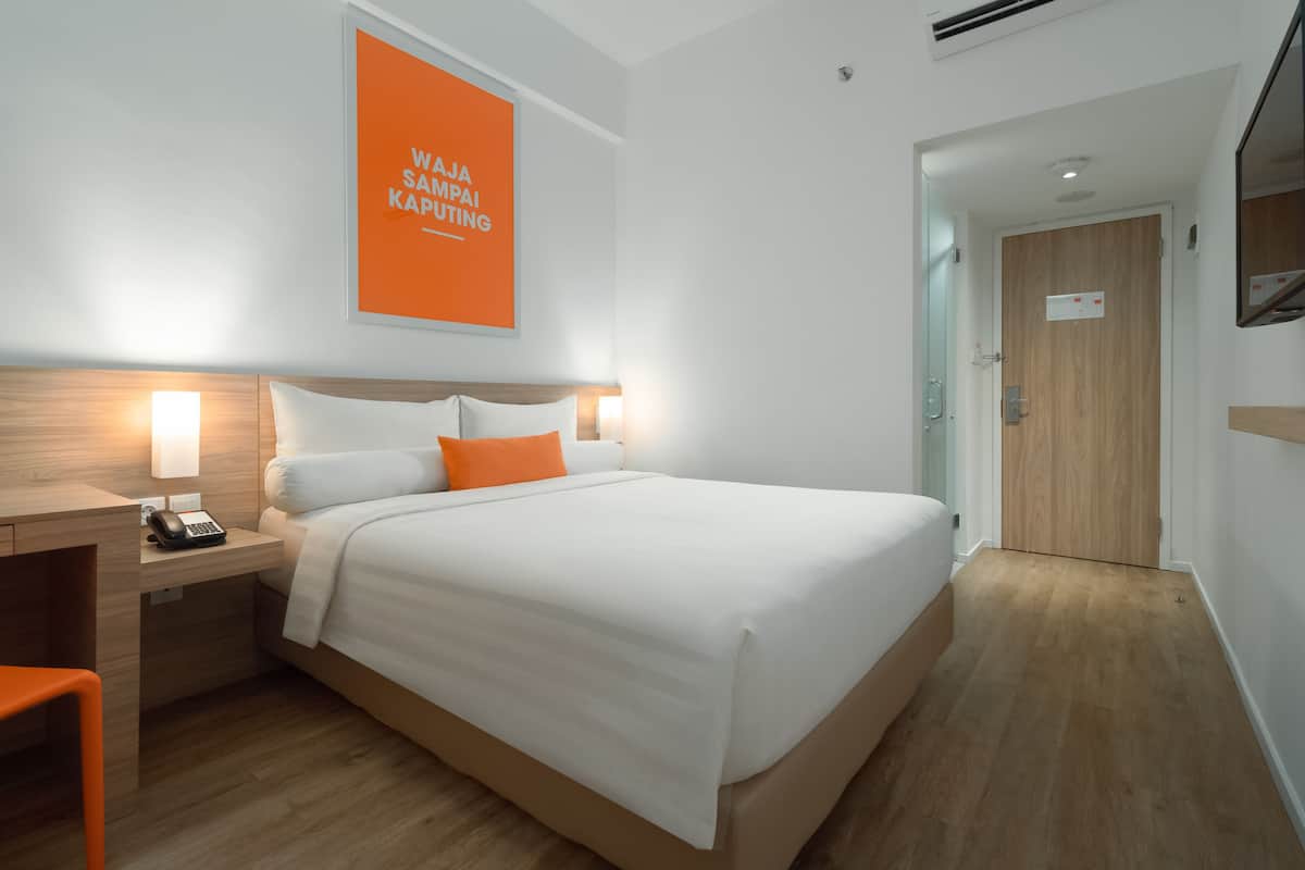 Een moderne hotelkamer met een groot bed, bedlampen, een houten nachtkastje en een feloranje bord aan de muur.