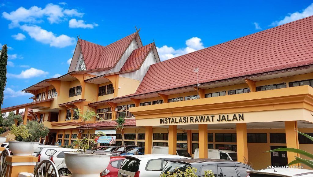 A building with a sign reading "INSTALASI RAWAT JALAN" and a parking lot with several cars.