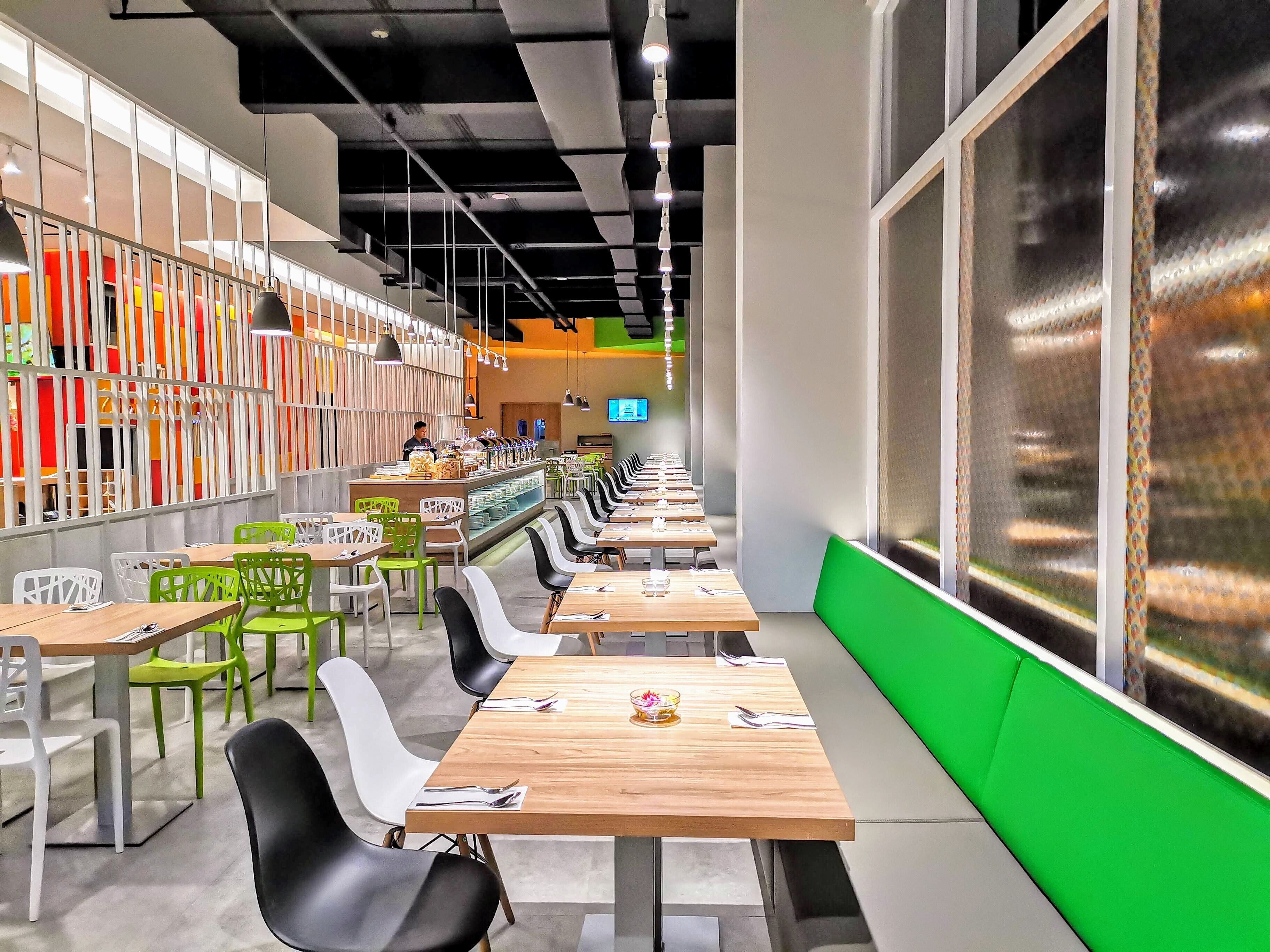 A modern cafeteria with long tables and chairs, a counter with food items, and a TV screen on the wall.