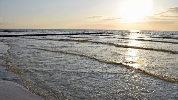 Une plage avec des vagues et un soleil couchant à l’horizon.