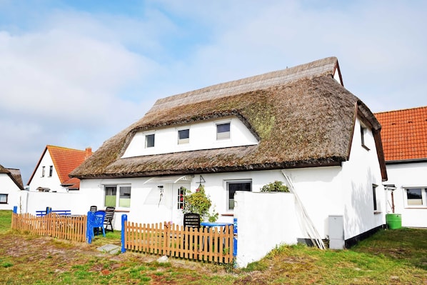 Une maison blanche avec un toit de chaume et une clôture en bois.