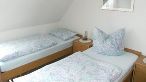 Ein kleines, schlichtes Zimmer mit zwei Einzelbetten, einem Nachttisch mit Lampe und einem Spiegel an der Wand.