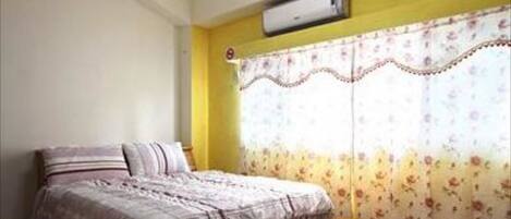 Quarto com cama, ar condicionado e janela com cortinas florais.