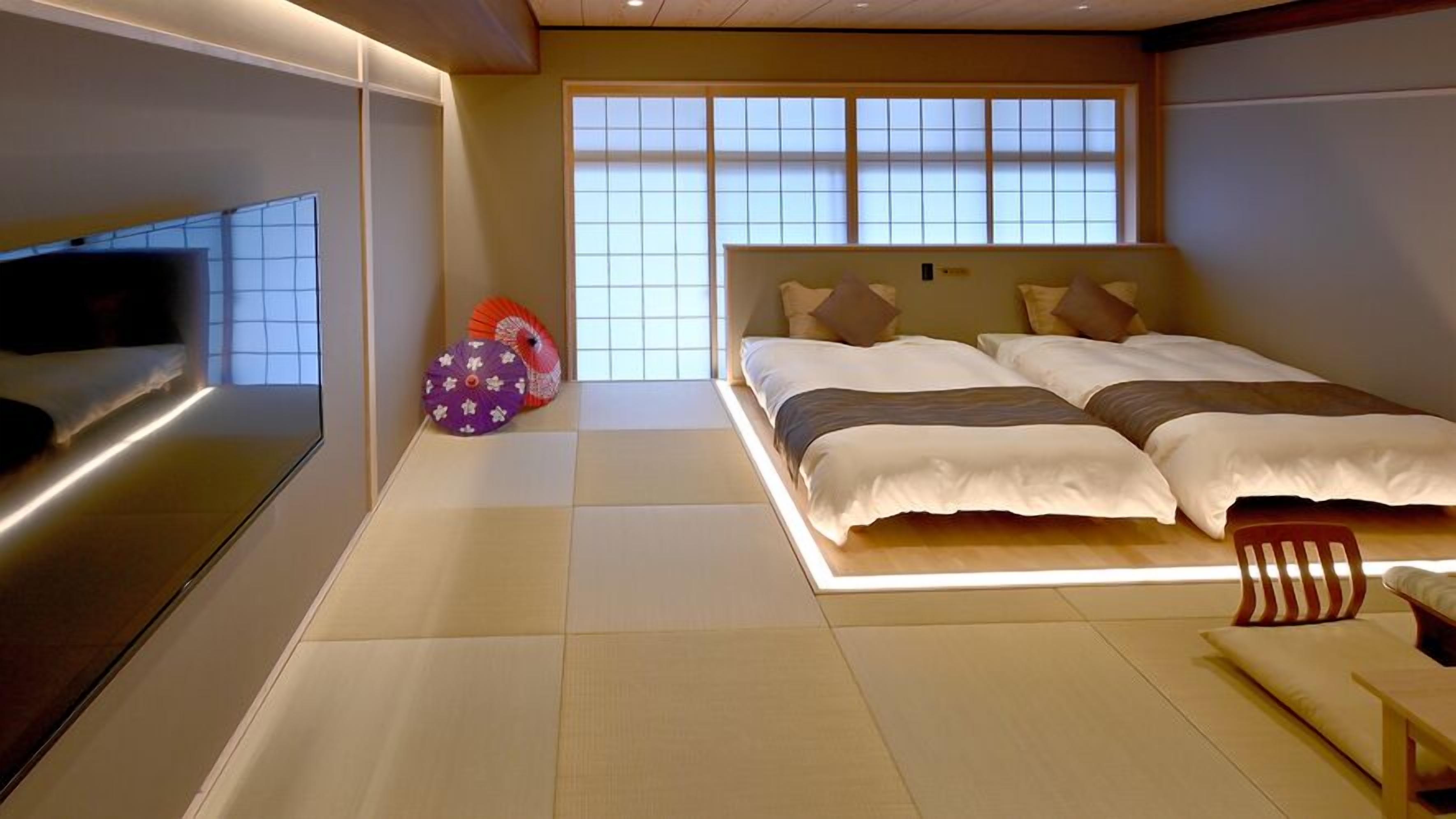 A modern hotel room with a large bed, a TV mounted on the wall, and a view of the city through large windows.