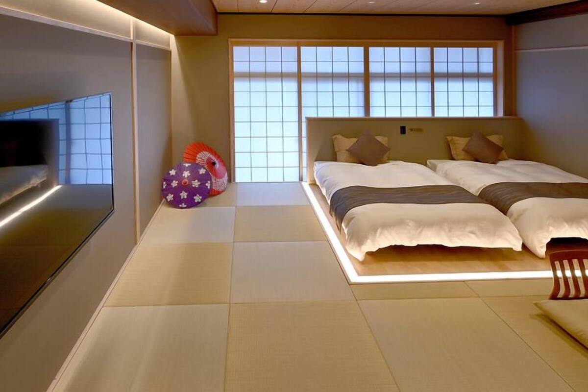 Habitación de hotel moderna con una cama grande, un televisor en la pared y vistas de la ciudad a través de amplias ventanas.
