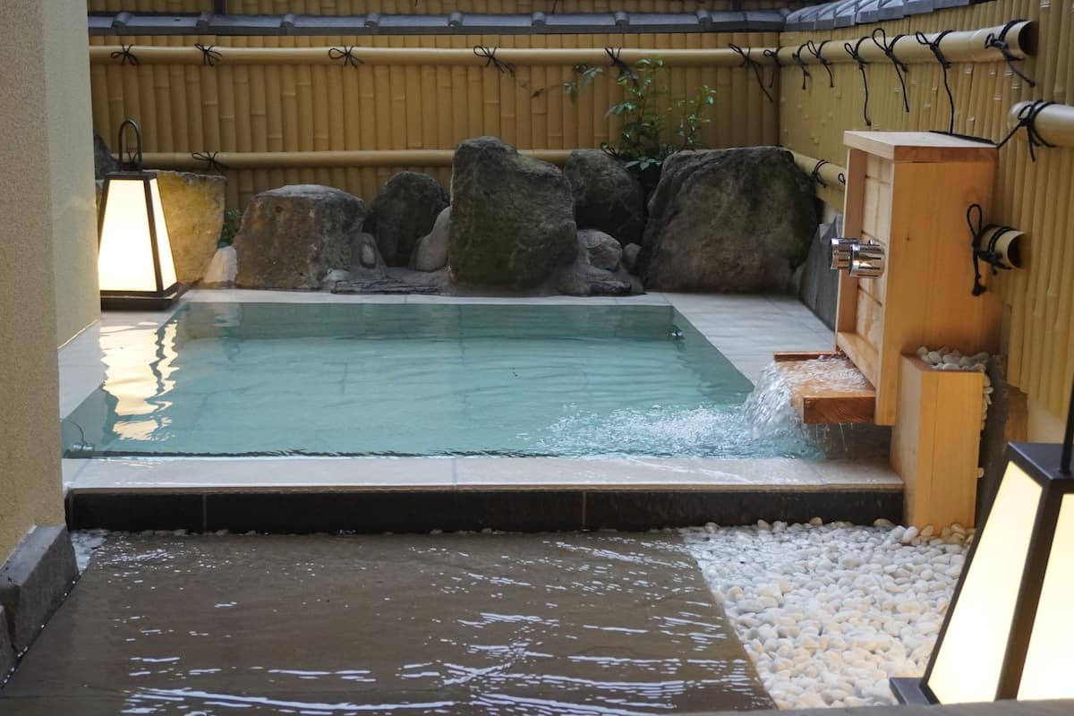 Un área de aguas termales con piscina, rocas y una estructura de madera.