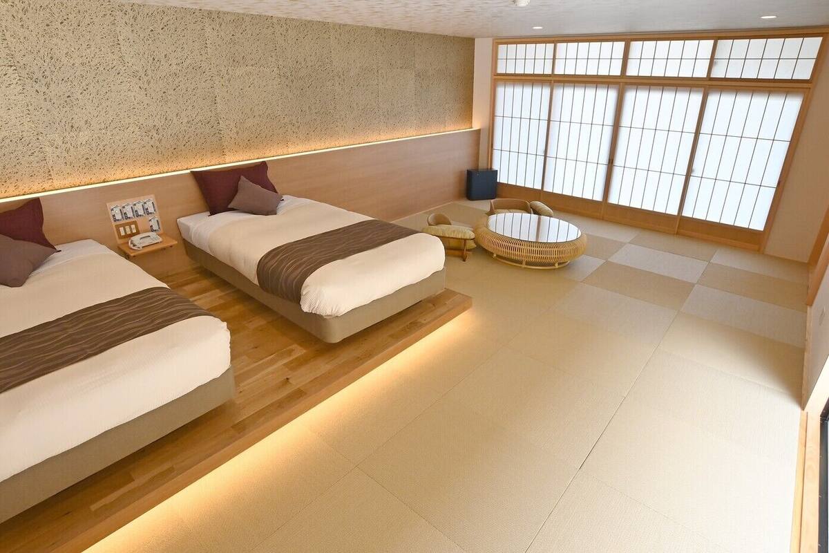Una habitación de hotel moderna con dos camas, una mesita redonda y un ventanal con vistas.