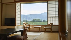 Une pièce de style japonais traditionnel, avec un sol recouvert de tatamis, une table basse, deux chaises et un téléviseur.
