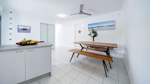 A modern kitchen with white cabinets, a wooden dining table, and a ceiling fan. - Best Location Welcoming Home (Buddina)