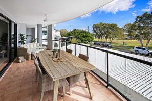 A balcony with a wooden table, wicker chairs, and a ceiling fan. - Cotton Tree Absolute Waterfront (Maroochydore)