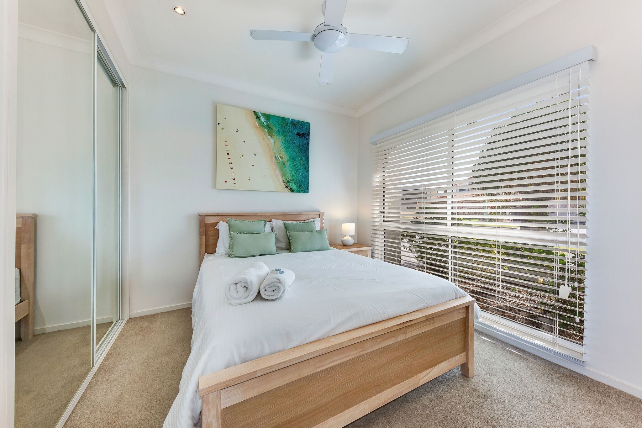 A bedroom with a bed, a ceiling fan, a window with blinds, and a painting on the wall.