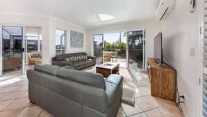 Una sala moderna con un sofá gris, una mesa de centro de madera y un televisor sobre un mueble de madera. Amplias ventanas permiten la entrada de luz natural y ofrecen vistas al exterior.
