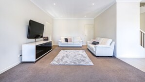 Un salon moderne avec un téléviseur à écran plat, un canapé blanc et un tapis gris.