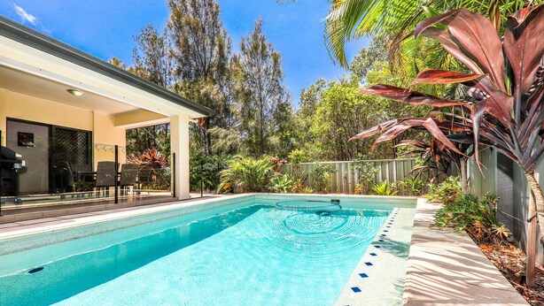 Une piscine rectangulaire à l’eau d’un bleu limpide, entourée d’une terrasse en béton et bordée d’un petit muret en pierre.