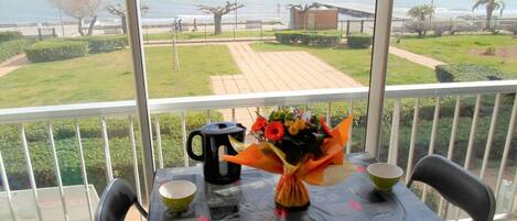 A balcony with a table set for two, a vase of flowers, a black kettle, and two bowls.