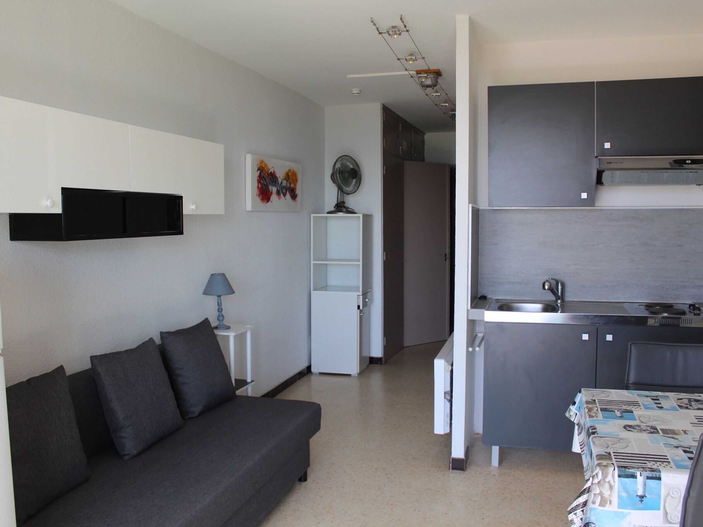 Espaço compacto com sofá, uma pequena mesa, cozinha compacta e porta para outro cômodo.