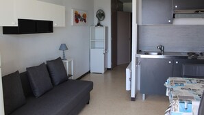 A compact living space with a sofa, a small table, a kitchenette, and a door leading to another room. - Air-conditioned apartment near the Thermal Baths in Balaruc-les-Bains (Balaruc-les-Bains)