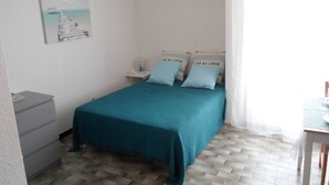 A bedroom with a bed, a nightstand, a lamp, a painting, and a window with curtains. - Studio near Balaruc Thermal Baths, Air-Con, Pets Allowed (Balaruc-les-Bains)