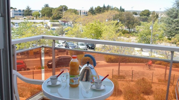 A balcony with a table set for two, a bottle of juice, and a kettle. - Studio near Balaruc Thermal Baths, Air-Con, Pets Allowed (Balaruc-les-Bains)