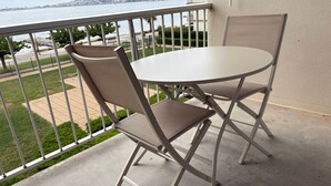 A balcony with a table and chairs, overlooking a body of water and a distant cityscape. - Cozy apt facing the pond, 2 stars, pets allowed (Balaruc-les-Bains)