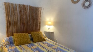 A bed with a patterned bedspread, two pillows, a bedside lamp, and a wall-mounted mirror. - Cozy apt facing the pond, 2 stars, pets allowed (Balaruc-les-Bains)