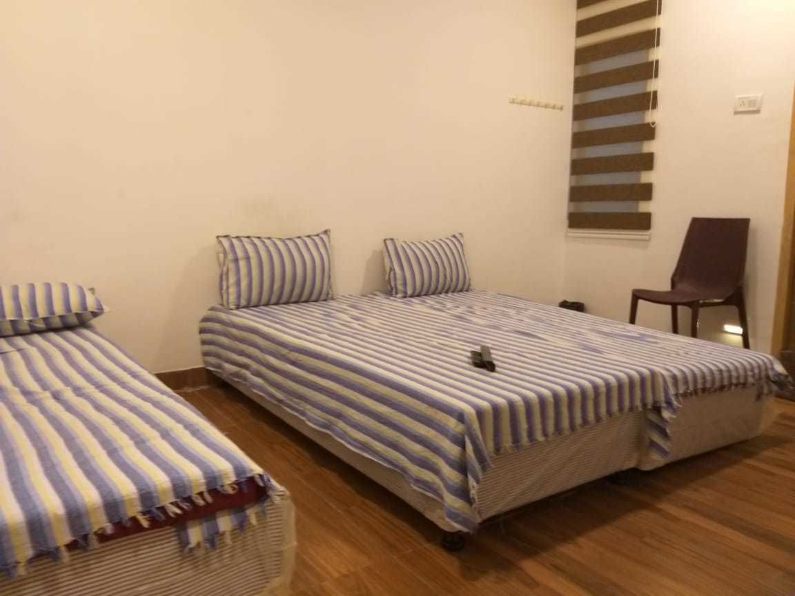 Quarto com duas camas de solteiro, uma cadeira e janela com persianas.