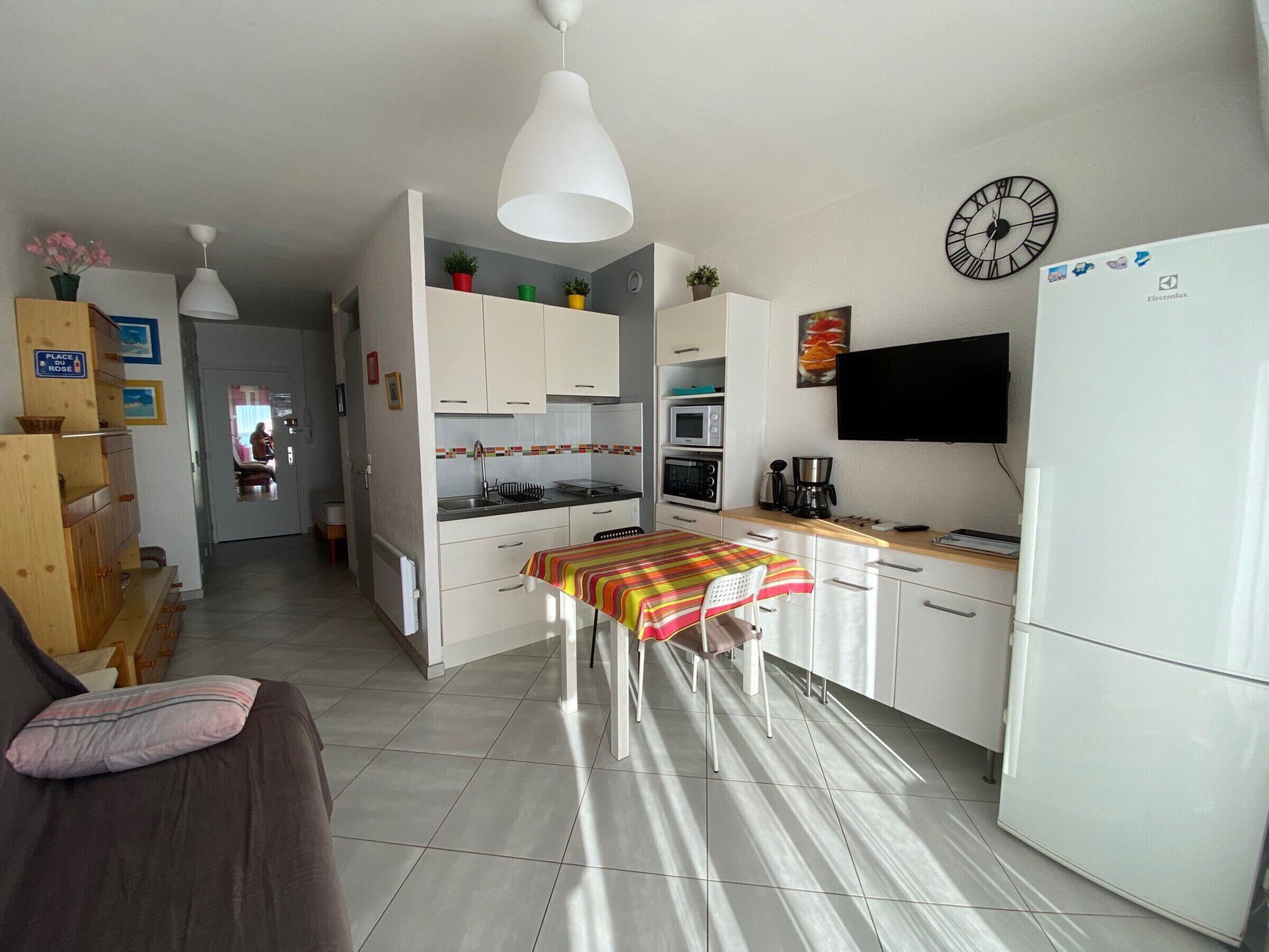 A compact kitchen with white cabinets, a microwave, an oven, a coffee maker, and a clock on the wall.