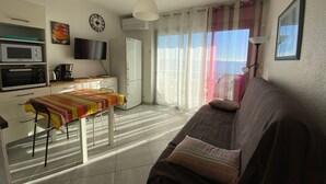 Un espacio habitable compacto con kitchenette, una mesa de comedor, un sofá y un amplio ventanal con cortinas.