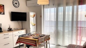 Una sala de estar moderna con comedor, televisor de pantalla plana y un amplio ventanal con cortinas traslúcidas.
