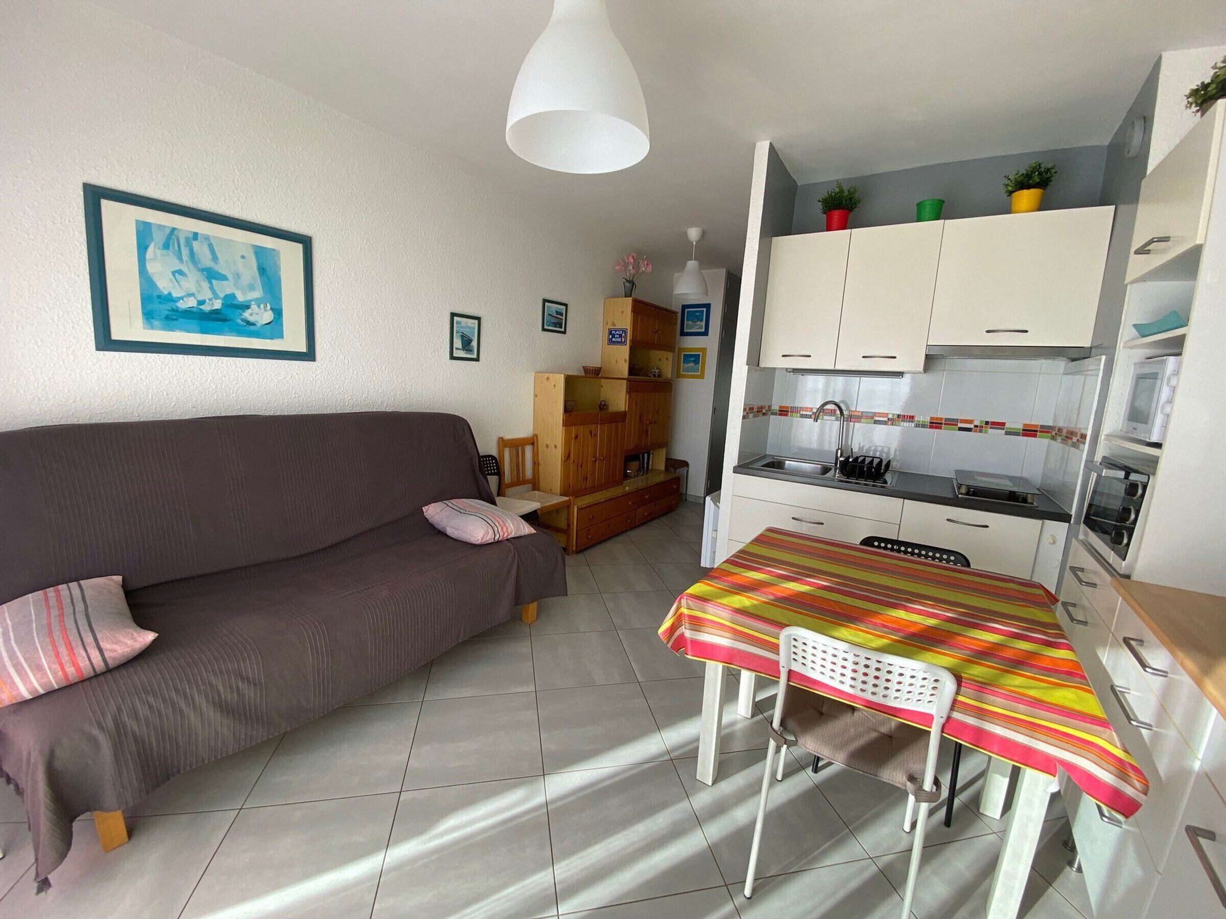 A compact living space with a sofa, a small dining table, a kitchenette, and a tiled floor.