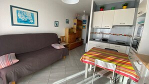Un espacio habitable compacto con sofá, una pequeña mesa de comedor, kitchenette y piso de baldosas.