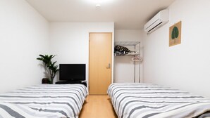 Une chambre avec deux lits, une télévision, une porte et une plante.
