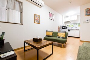 Un espace de vie compact comprenant un canapé, une petite table et un coin cuisine à l’arrière-plan.