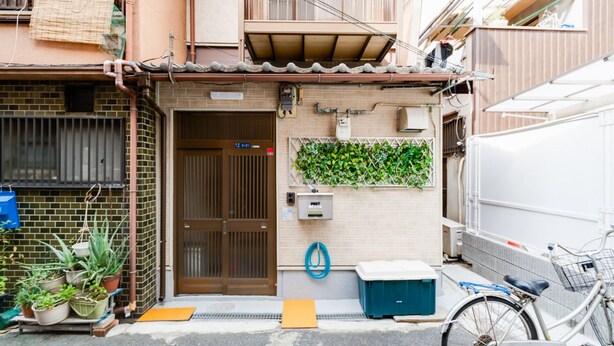 Une rue étroite en milieu urbain, avec un petit bâtiment doté d’une porte marron, d’un mur végétal vert et d’un vélo garé à l’extérieur.