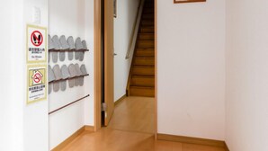 Un couloir avec un porte-chaussures, un panneau indiquant « chaussures interdites », une affiche de Spiderman et un escalier menant à une autre pièce.