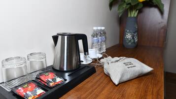 A coffee station with a kettle, cups, and packets of coffee. There are also water bottles and a vase with flowers on the table.