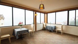 A room with large windows, a table with a vase of flowers, and two chairs. - Sapa Symphony Hotel (Sa Pa)