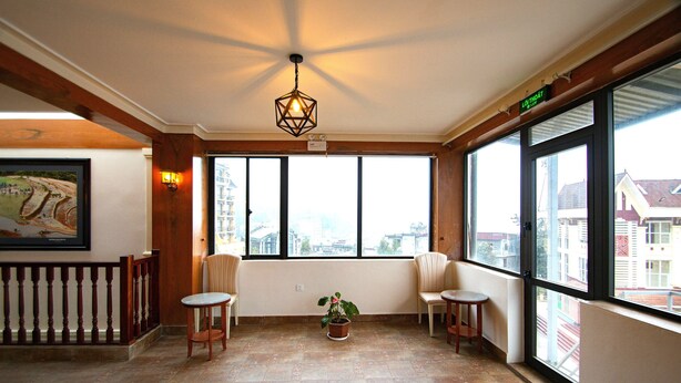 A spacious balcony with large windows, a potted plant, and two chairs. - Sapa Symphony Hotel (Sa Pa)