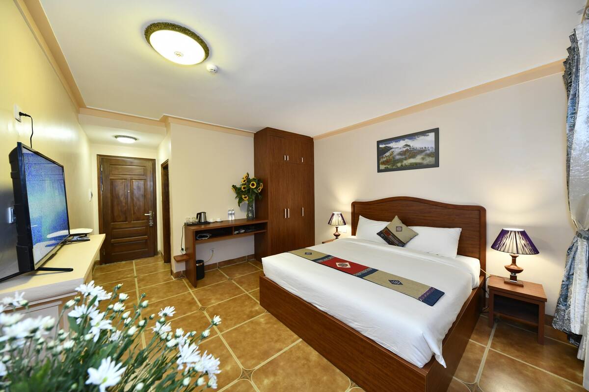 Habitación de hotel con una cama grande, un escritorio con computadora, televisor y una mesita de noche con lámpara.