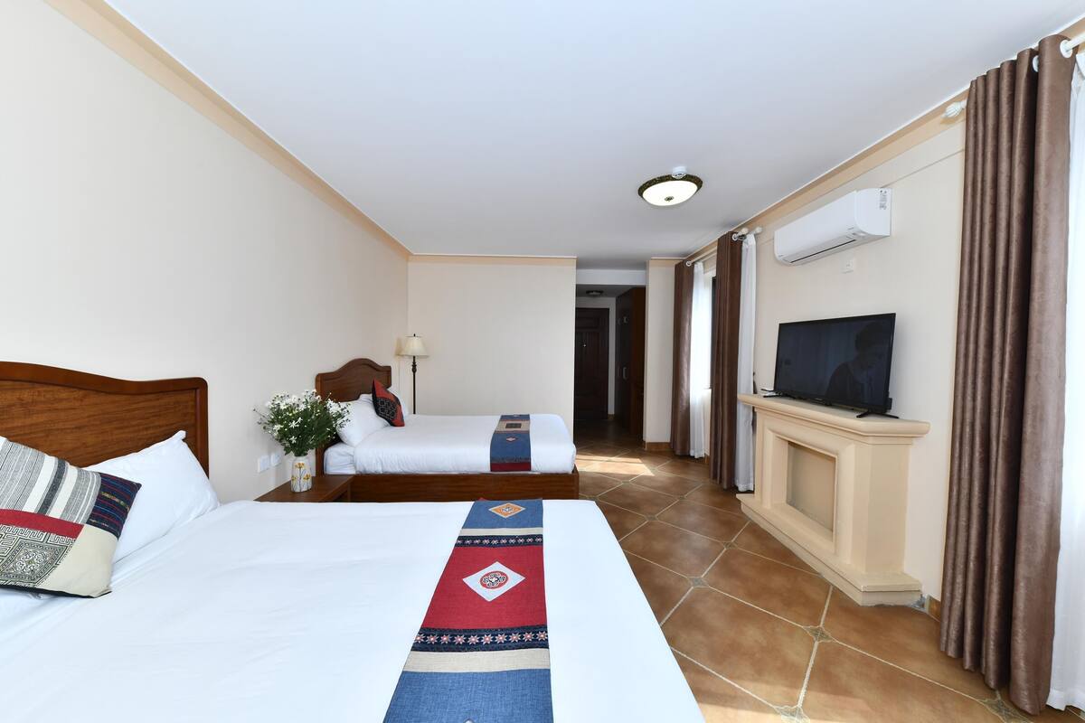 Una habitación de hotel con una cama grande, otra más pequeña, un televisor y un equipo de aire acondicionado.