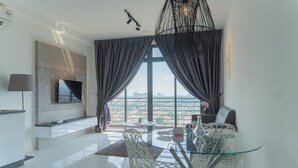 A modern living room with a glass table, white chairs, a mounted TV, and a city view through large windows. - OYO Home 43995 Premium 3br 1tebrau (Johor Bahru)