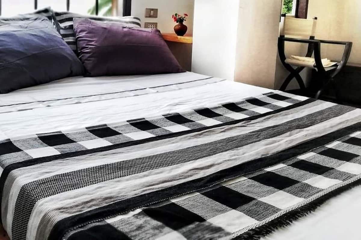 A bed with a checkered bedspread, a nightstand with a vase, and a chair by a window.